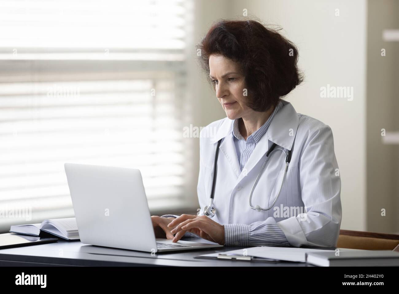 Konzentrierte Ärztin mittleren Alters, die am Computer arbeitet. Stockfoto