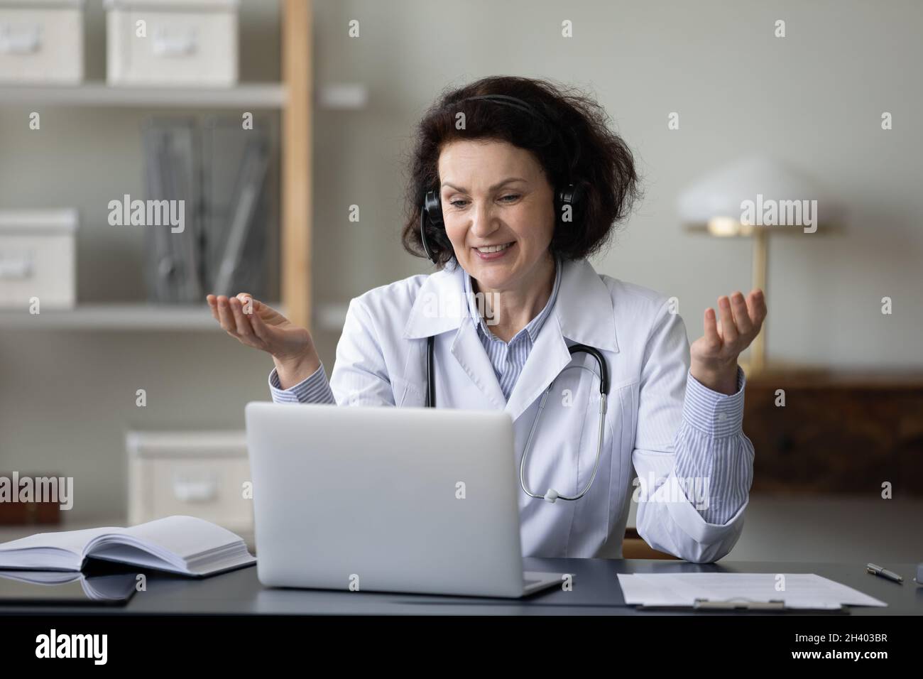 Lächelnde Ärztin mittleren Alters, die die Patientin per Videoanruf konsultiert. Stockfoto