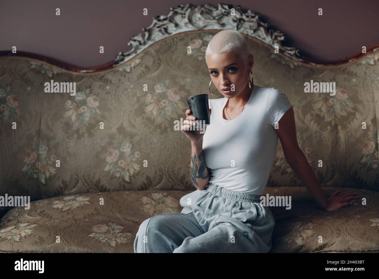 Eine junge Frau aus der Jahrtausendzeit mit kurzen blonden Haaren sitzt auf einem Vintage-Sofa. Stockfoto