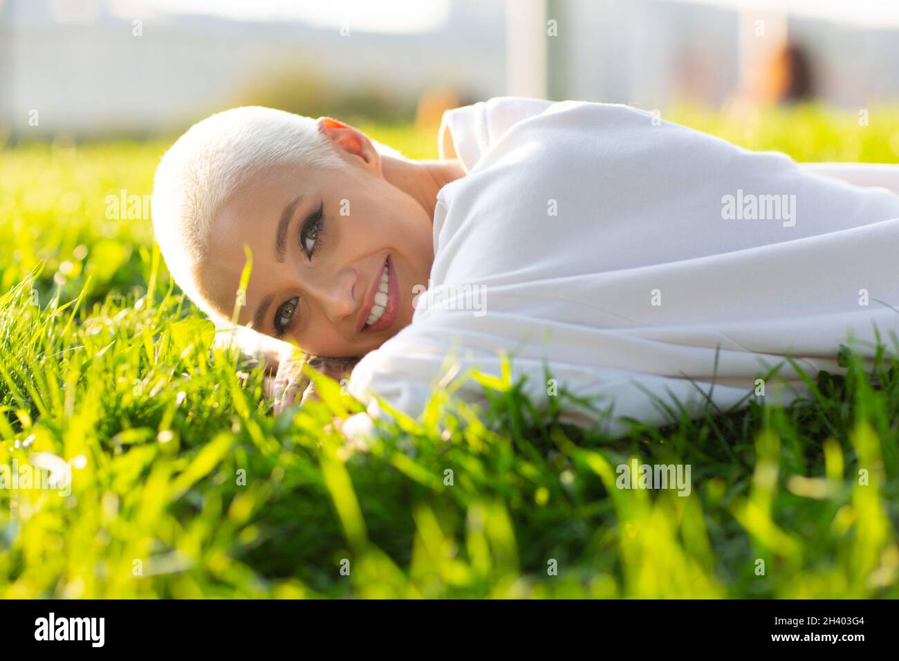 Millenial junge Frau blond kurze Haare im Freien lächelnd lag auf Gras Porträt. Stockfoto