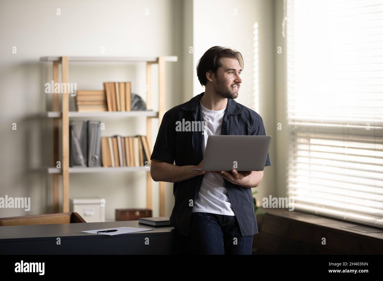 Verträumter junger Geschäftsmann, der Computer in den Händen hält. Stockfoto