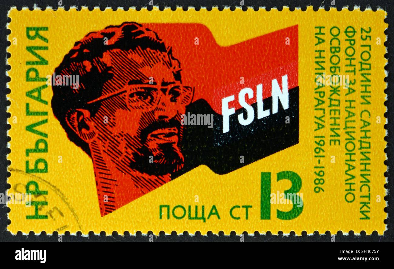 BULGARIEN - UM 1986: Eine in Bulgarien gedruckte Briefmarke zeigt Augusto Cesar Sandino (1893-1934), den nicaraguanischen Revolutionär, und die Flagge der sandinistischen Bewegung Stockfoto