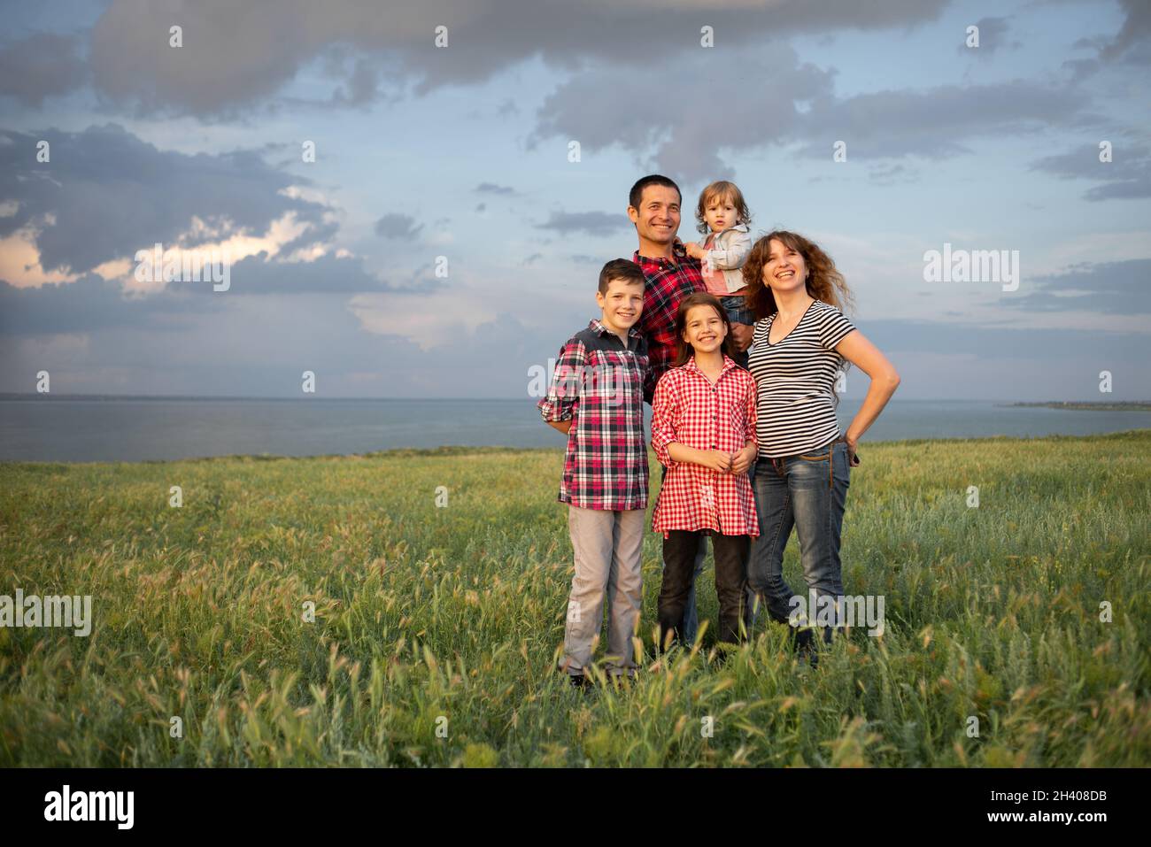 Fröhliche, freundliche große Familie mit drei Kindern zwei Söhne und eine Tochter stehen im Sommer bei Sonnenuntergang vor dem Hintergrund des wolkenblauen Himmels am Abend. Stockfoto