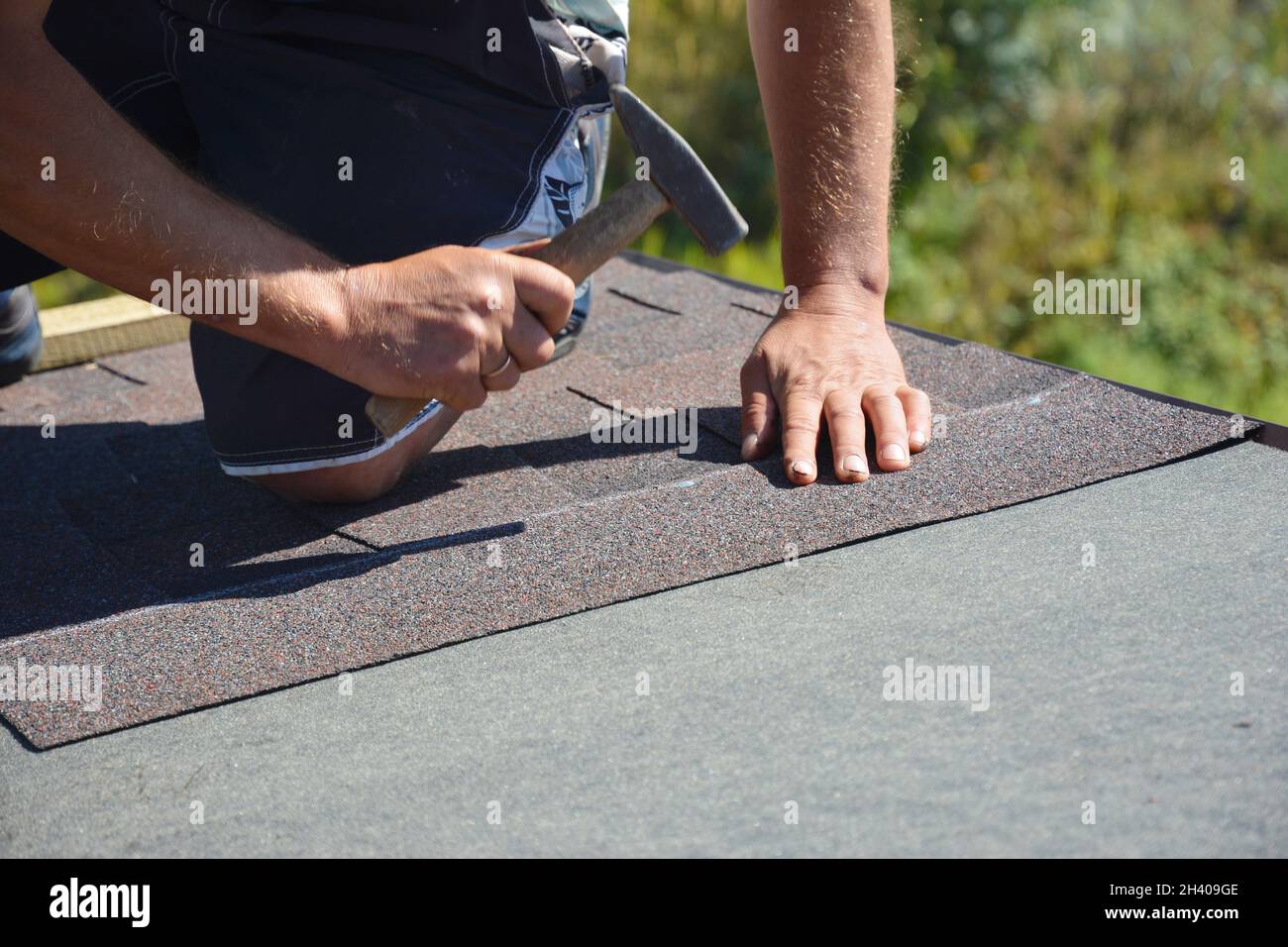 Dachkonstruktion. Dachdecker Installation Asphalt Schindeln auf Hausbau Dachecke mit Hammer und Nägel. Stockfoto