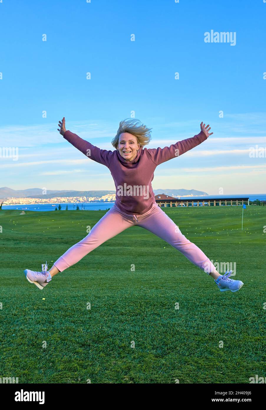 Glückliches Mädchen Golfer springen in der Luft mit erhobenen Armen und Golfschläger in der Hand nach erfolgreichem Schuss. Stockfoto