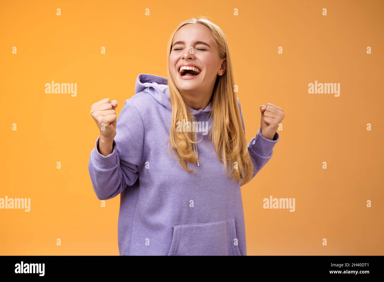 Süß glücklich triumphierende blonde europäische Mädchen im Hoodie brüllend ja erfüllen Traum Leben Klenchfäuste glücklich tanzen Zelebrati Stockfoto