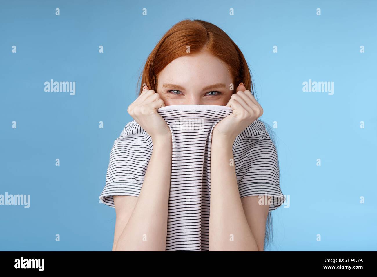 Alberne Flirty amüsiert attraktive verspielte Rotschopf Freundin versteckt Gesicht ziehen T-Shirt Kopf schielend hinterhältig mysteriös kichern Stockfoto