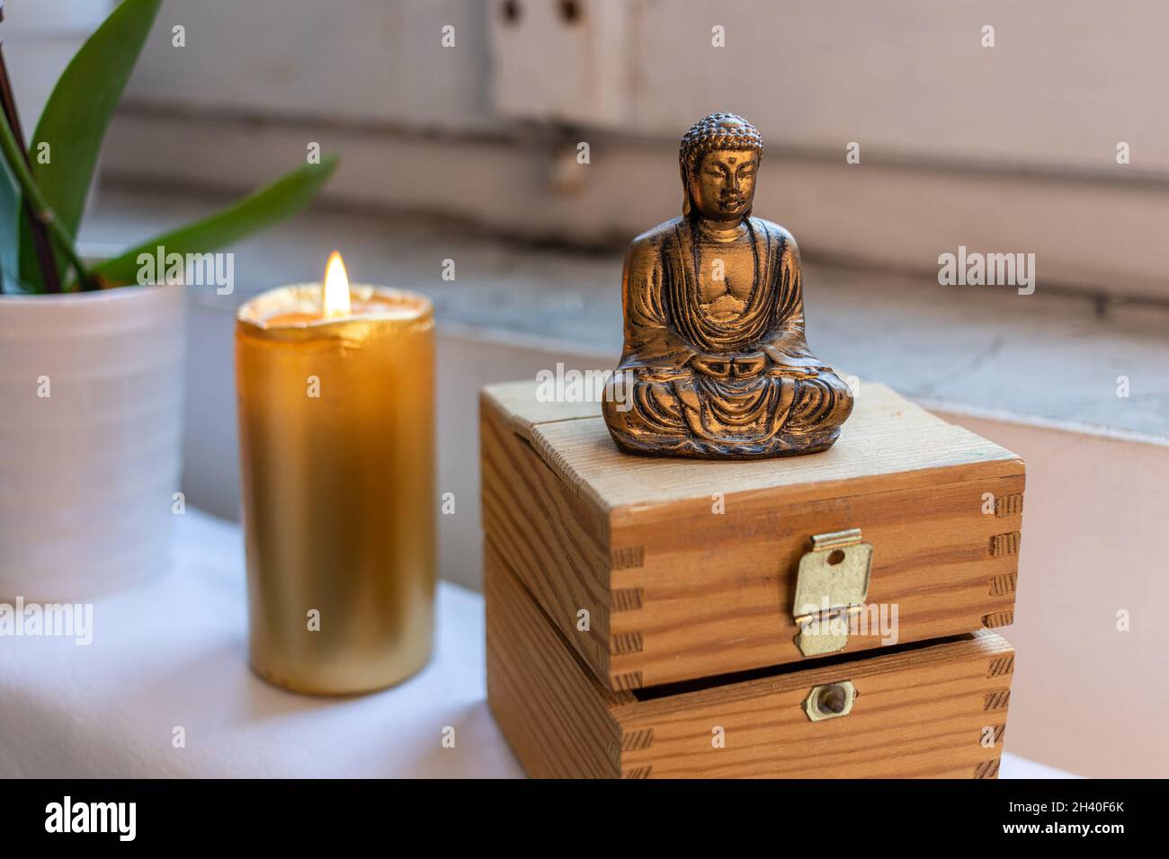 Zen Buddha Statue sitzend meditierend auf weißem Hintergrund. Kerzenlicht Steine und Brust im Hintergrund Stockfoto