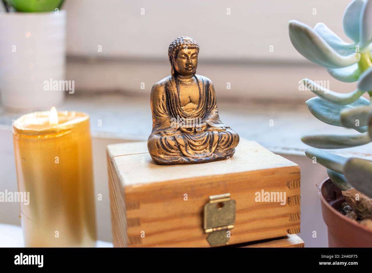 Zen Buddha Statue sitzend meditierend auf weißem Hintergrund. Kerzenlicht Steine und Brust im Hintergrund Stockfoto