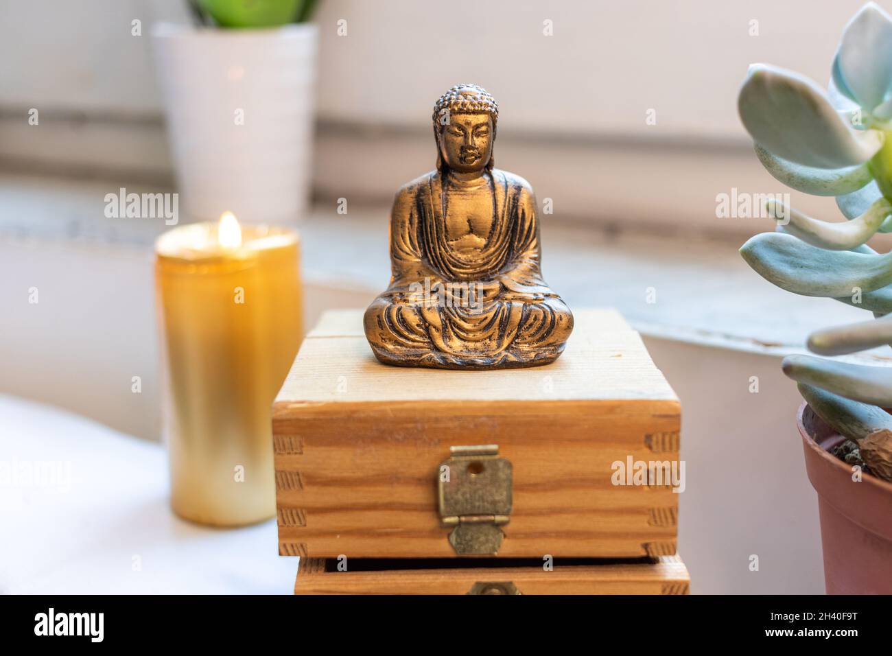 Zen Buddha Statue sitzend meditierend auf weißem Hintergrund. Kerzenlicht Steine und Brust im Hintergrund Stockfoto