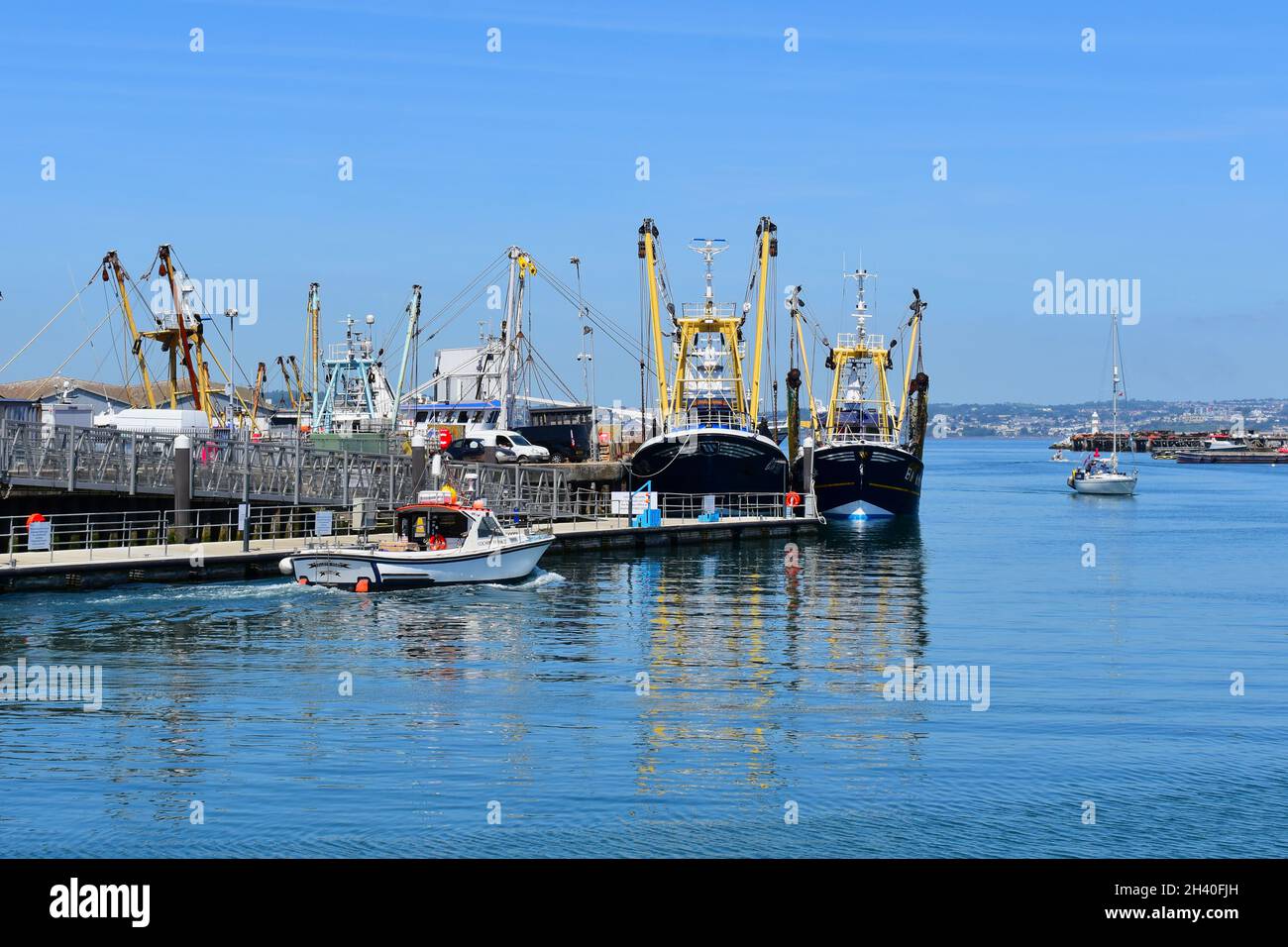 Eine Szene von größeren Seeschleppern, die am Hafen in Brixham festgebunden sind. Vergnügungsboote kommen und fahren durch den Haupteingang des Hafens. Stockfoto