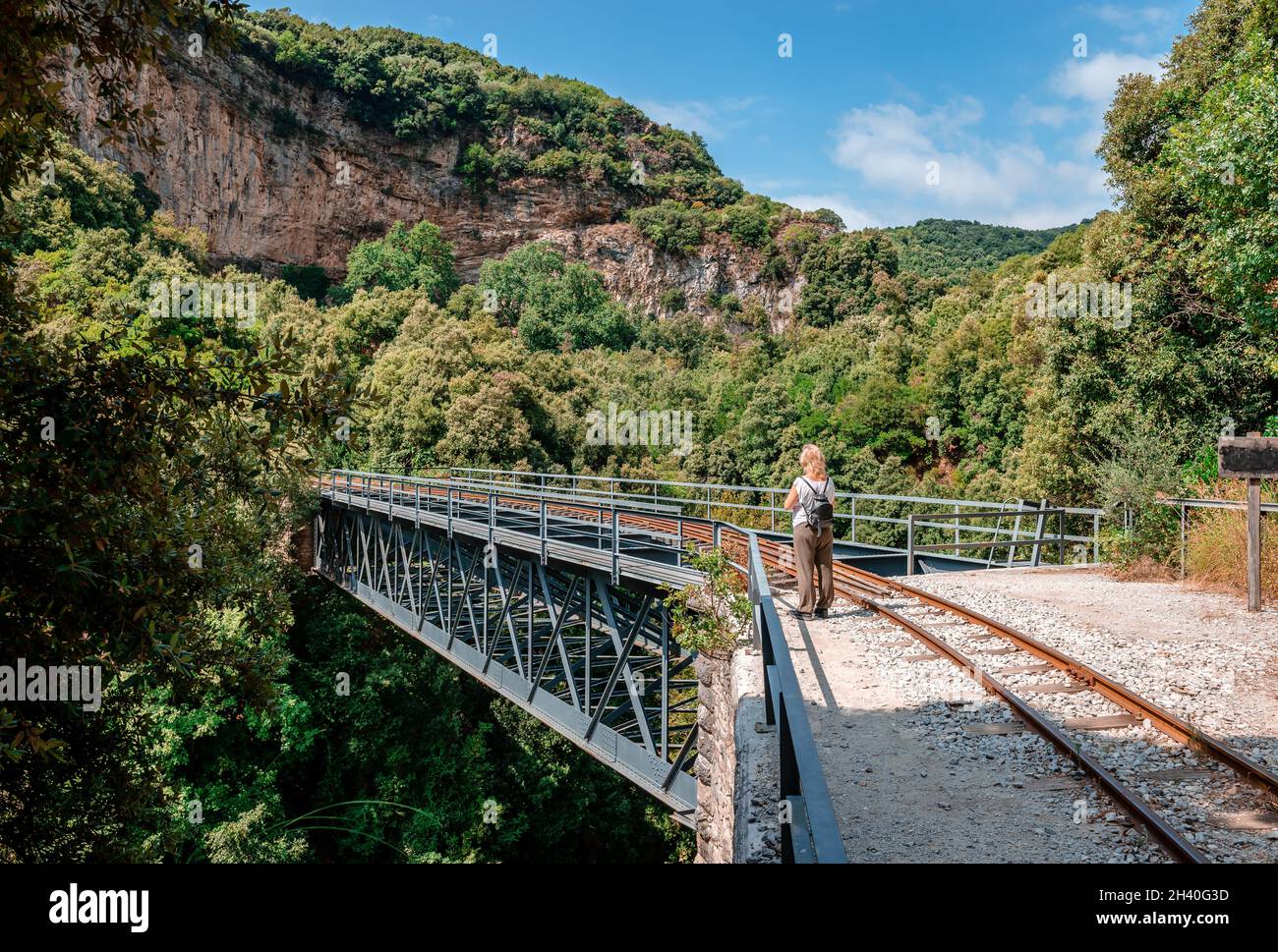 Rückansicht einer blonden kaukasischen Frau, die in der historischen Brücke von Taxiarchis (alias De Chirico's) in der Nähe des Bahnhofs Milies im Berg Pelion, Griechenland, steht. Stockfoto