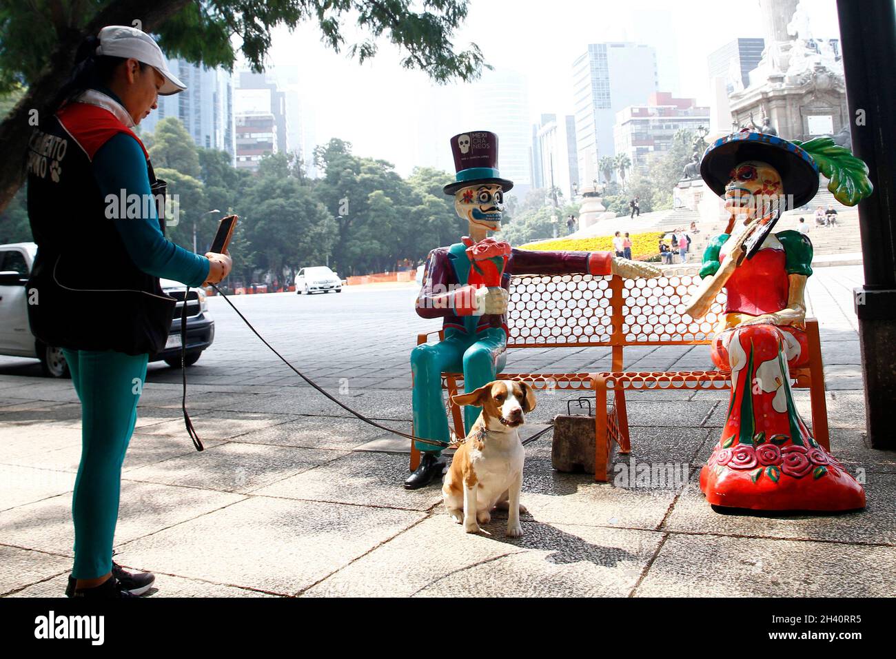 Non Exclusive: Eine Frau fotografiert ihren Hund vor einer Catrina, die aus Pappe hergestellt wurde, die als Teil des Dia de die Hauptstraßen schmückt Stockfoto