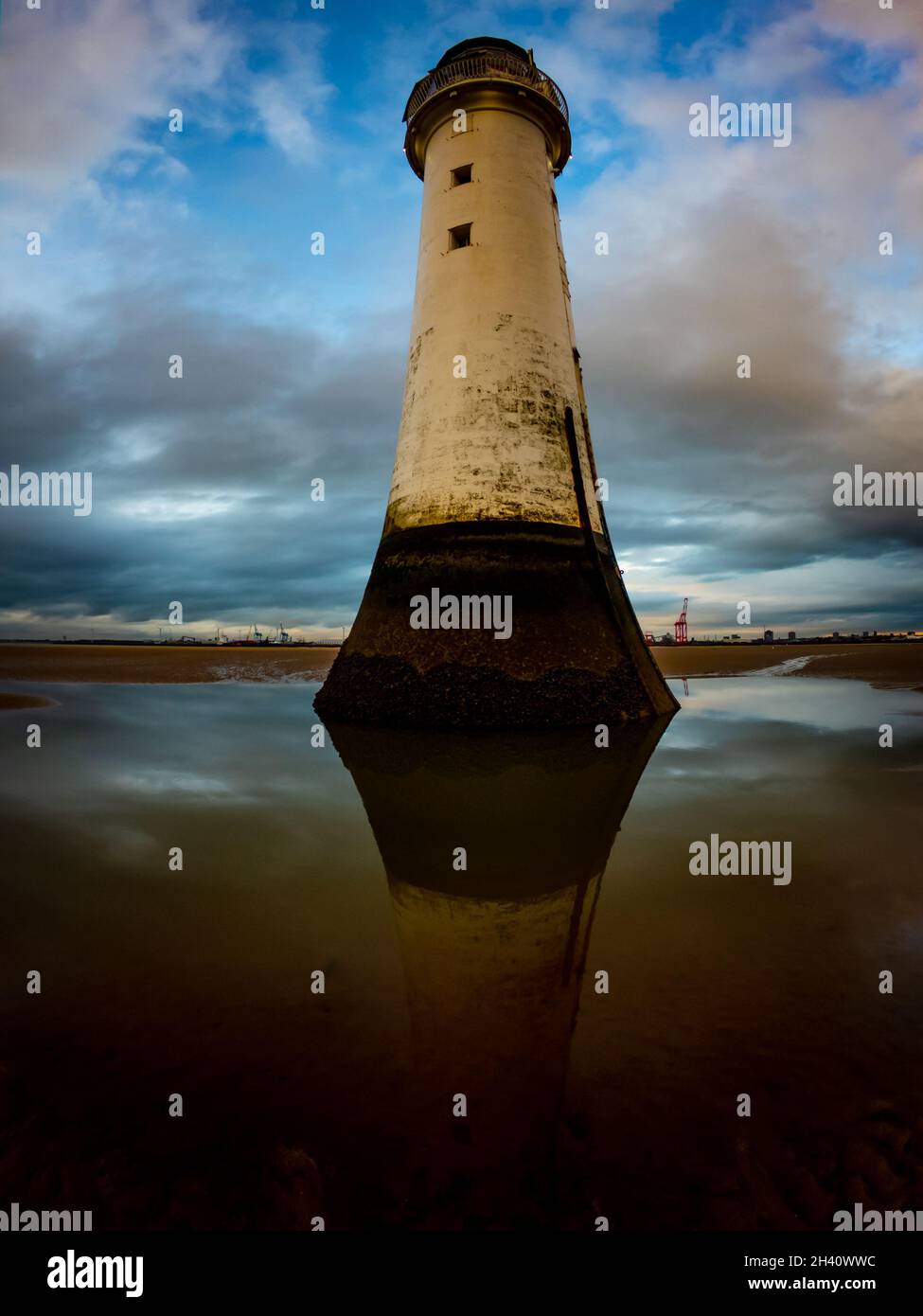 Leuchtturm und seine Reflexion im Wasser auf einem Sandstrand in der Nähe von Wallasey, Wirrall gegen einen blauen und bewölkten Himmel. Stockfoto