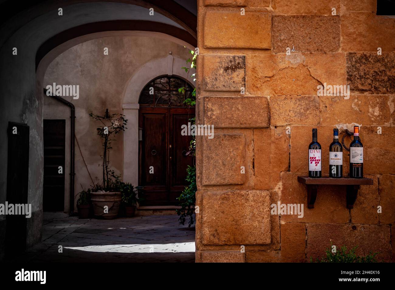 Flaschen Rotwein auf einer rustikalen Fassade in Italien mit traditionellen Torbögen und mediterranem Luxuskonzept Stockfoto