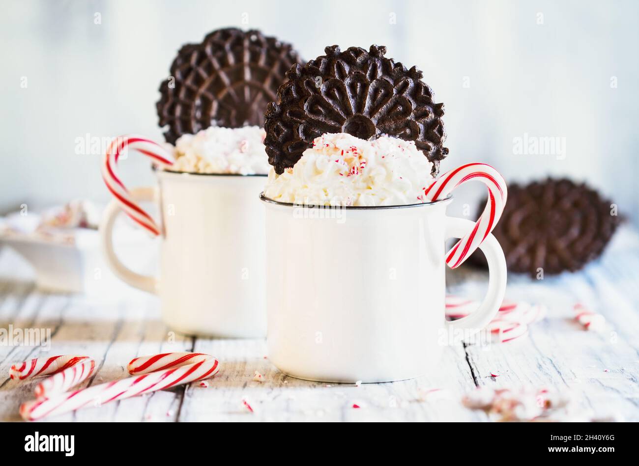 Zwei Tassen heißen Kakao mit Schlagsahne, zerdrückten Zuckerstöcken und Pizzelle Plätzchenwafern für Weihnachten. Selektiver Fokus mit verschwommenem Vordergrund. Stockfoto