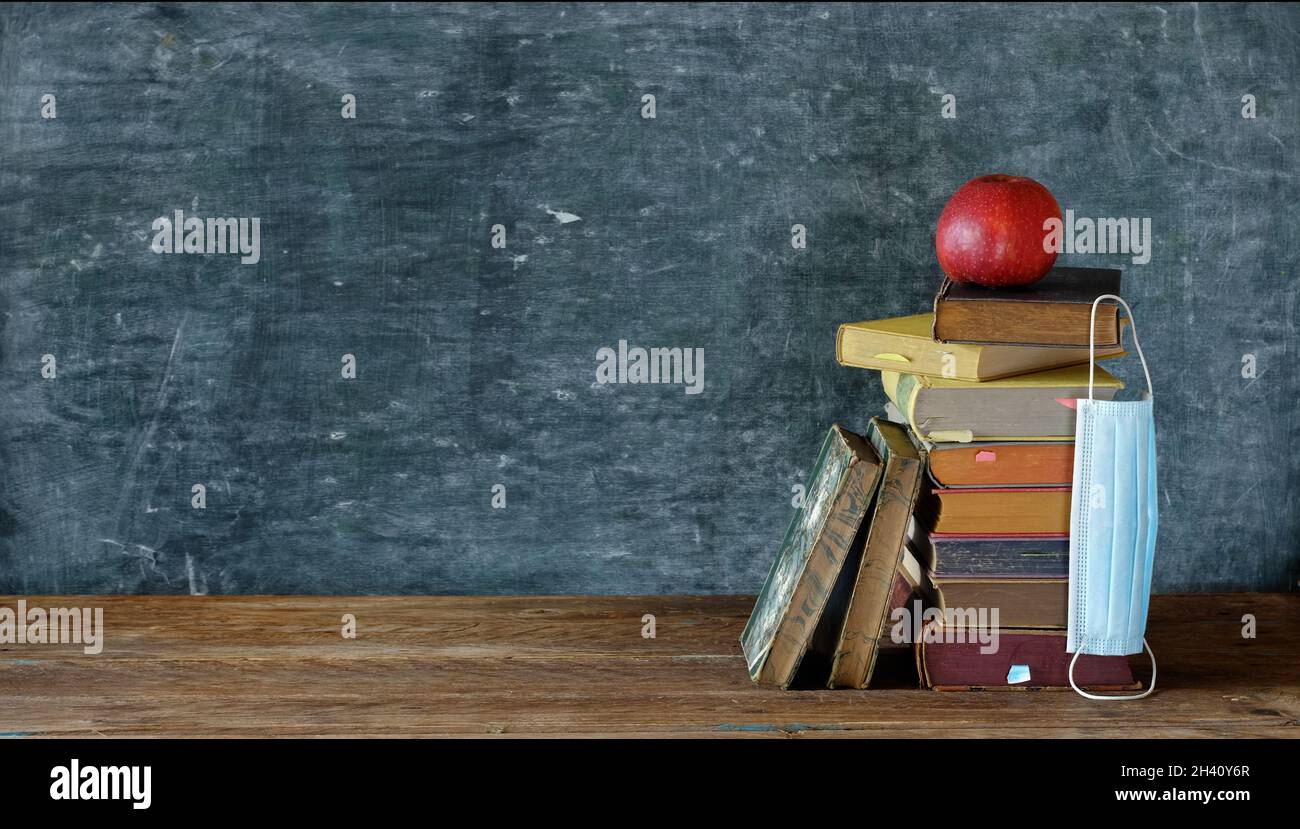 Zurück in die Schule in Zeiten der Corona, Anstecken von Büchern, Apfel- und corna-Maske vor der Schulschwarzen Tafel, freier Kopierplatz Stockfoto