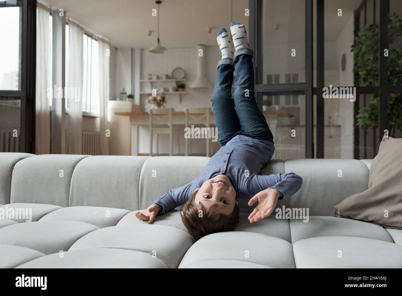Glücklicher kleiner Junge der 7er, der auf dem bequemen Sofa auf dem Kopf lag. Stockfoto