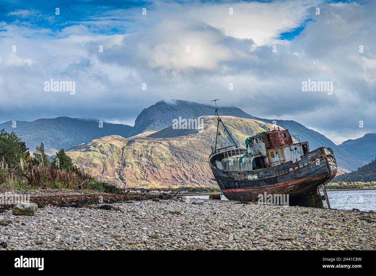 Verlassene Fischerboot in Corpach am Strand von Loch Linnhe in Fort William in den schottischen Highlands, hier mit Ben Nevis in der Ferne gesehen Stockfoto