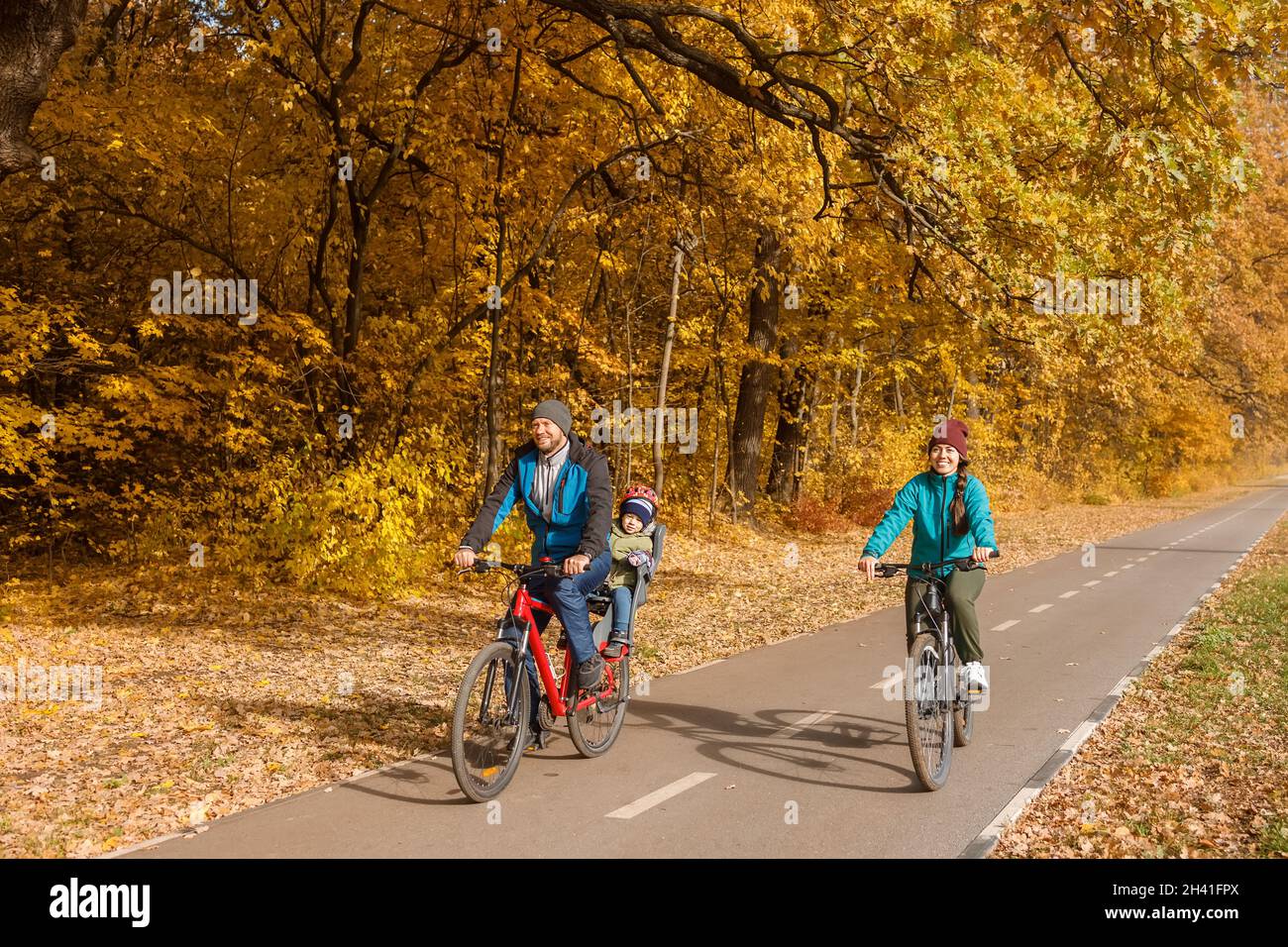 Familie mit Kind, die gemeinsam im Herbstpark auf Fahrrädern reitet Stockfoto