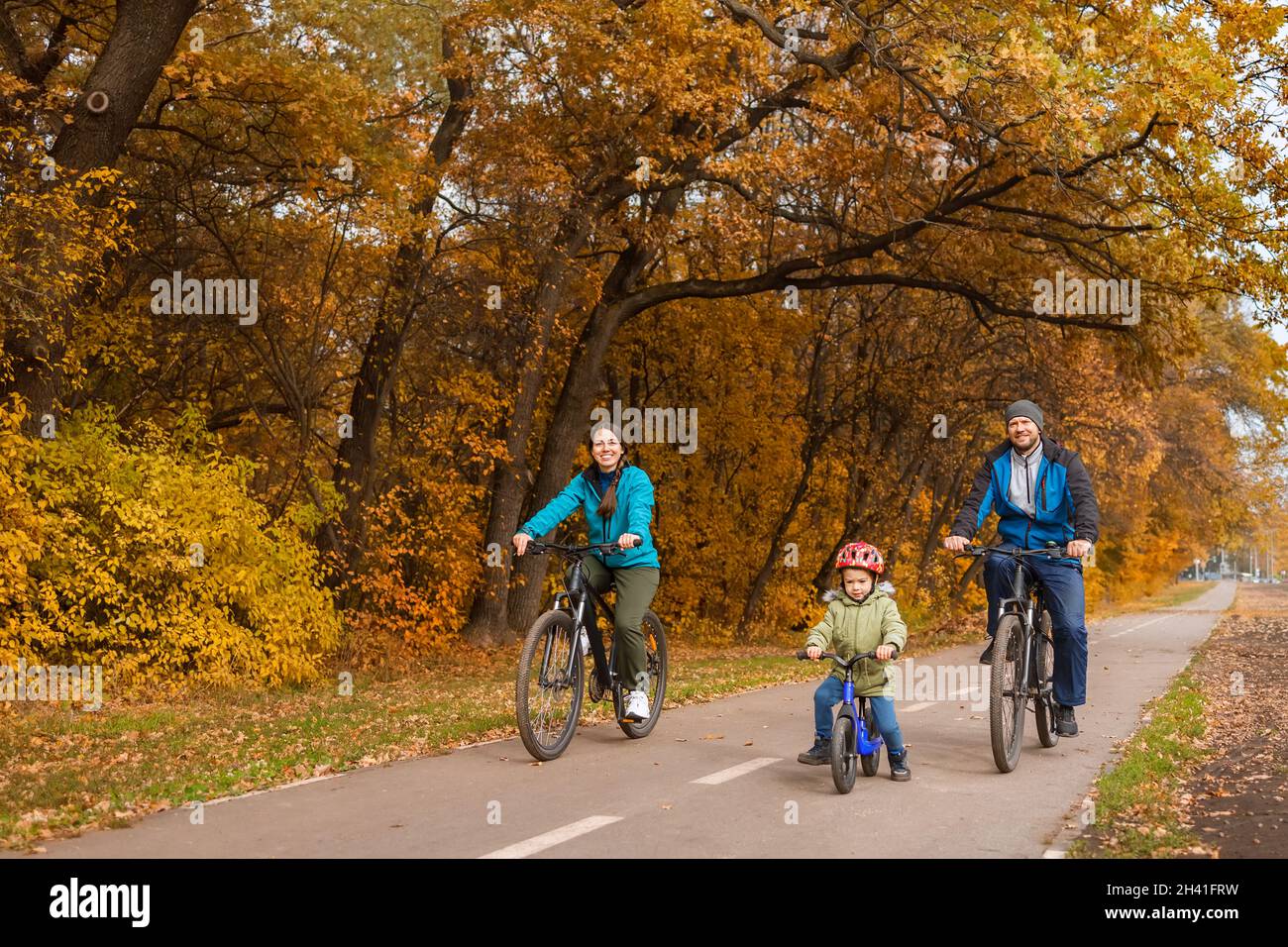 Familie mit Kind, die gemeinsam im Herbstpark auf Fahrrädern reitet Stockfoto