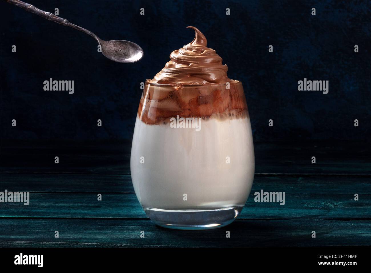 Dalgona kalter Kaffee in einem Glas mit einem Löffel, auf dunklem Grund Stockfoto