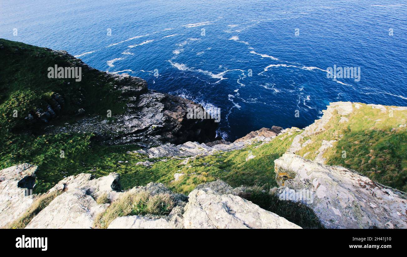 Kornische Klippe fällt in Richtung Meer, kontrastierende Felsformationen, Pflanzen Life Greens gegen das tiefe Blau des offenen Ozeans. Stockfoto