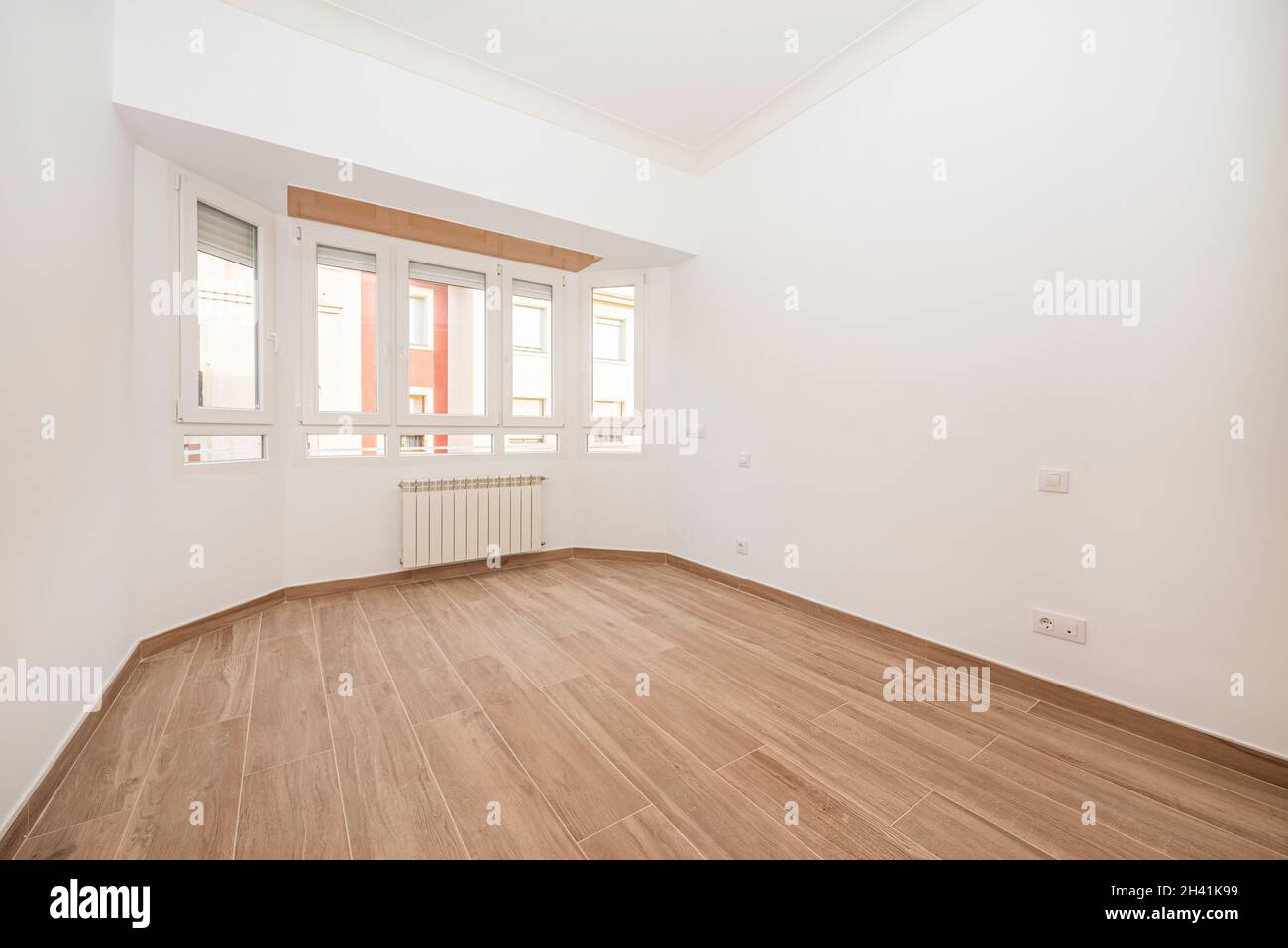 Weiß gestrichenes Zimmer mit Steinzeugboden wie Holz mit gebogenem Fenster und Aluminiumheizkörper Stockfoto