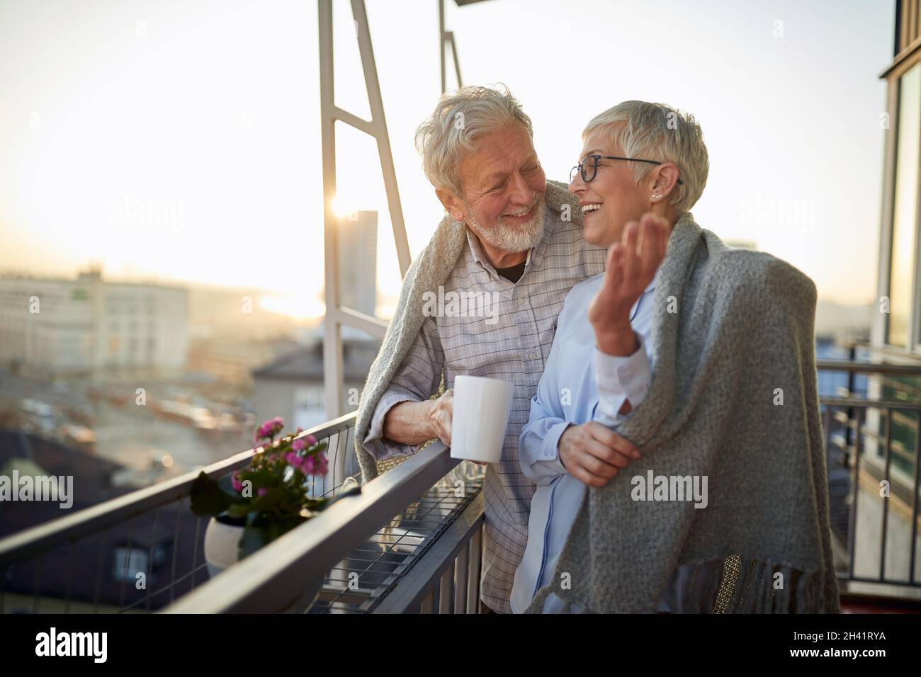 Ein älteres Paar plaudert und genießt einen schönen Sonnenuntergang von der Terrasse in einer entspannten Atmosphäre ihrer Wohnung. Beziehung, Liebe, zusammen Stockfoto