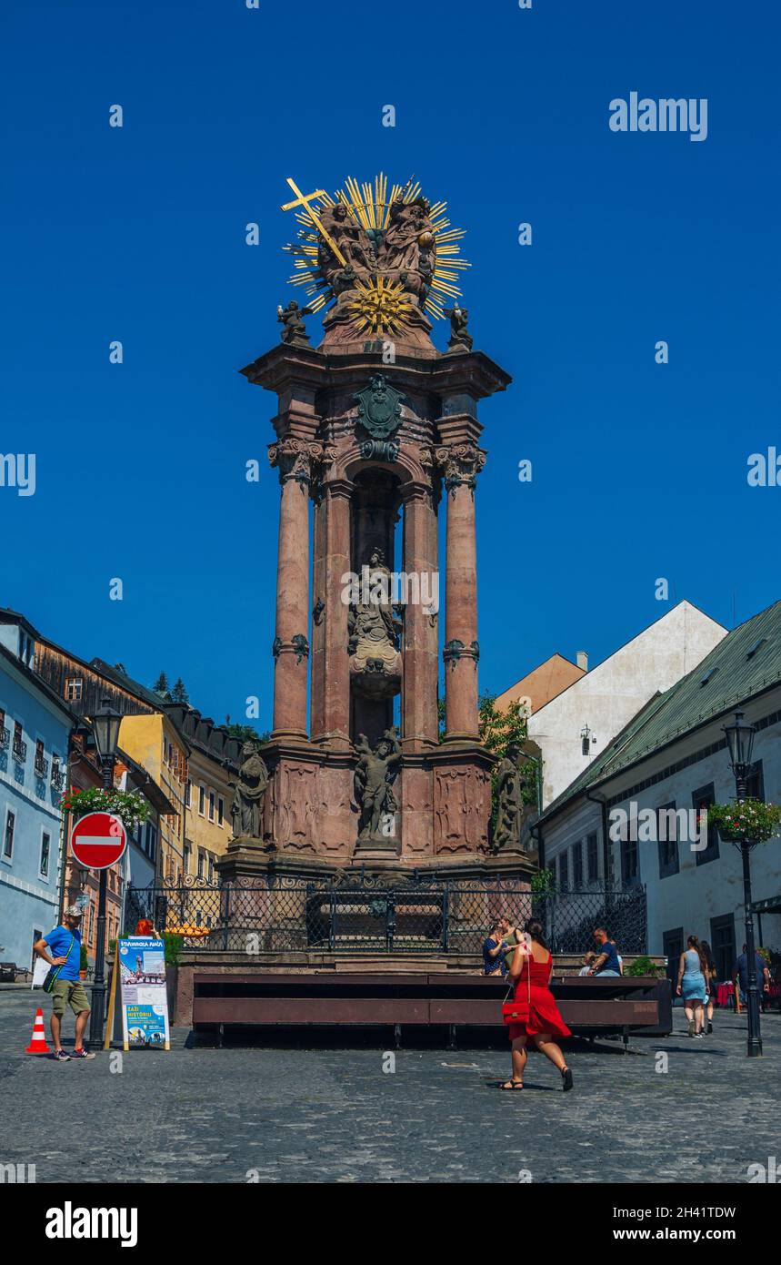 Banska Stiavnica, Slowakei – 14. August 2021: Blick auf die monumentale Pestsäule am Trinity Square über den blauen Himmel, alte historische Architektur und Touristen Stockfoto