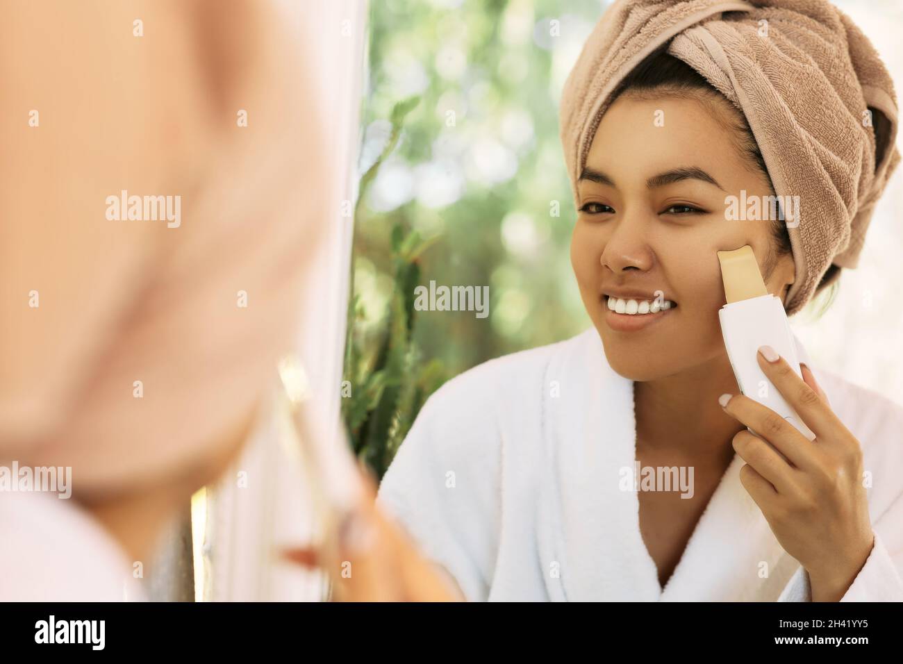 Gesichtshaut reinigen, Mitesser im Gesicht entfernen. Asiatische Frau Blick auf Reflexion im Spiegel, während Ultraschall Haut schälen Verfahren Stockfoto
