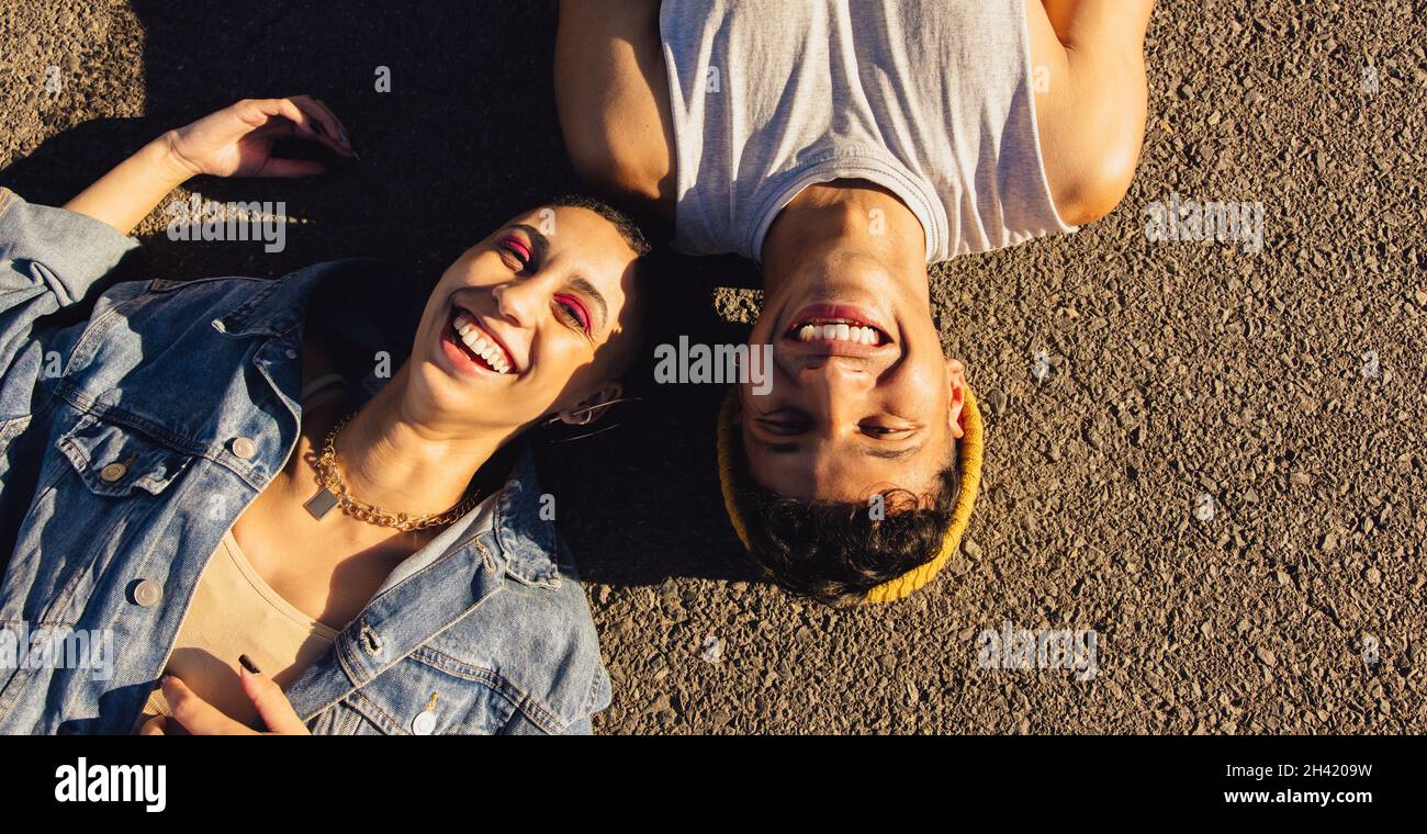 Draufsicht auf zwei glückliche Freunde, die auf der Straße liegen. Zwei Jugendliche lächeln fröhlich, während sie draußen unter der Sonne liegen. Beste Freunde der Opposposi Stockfoto