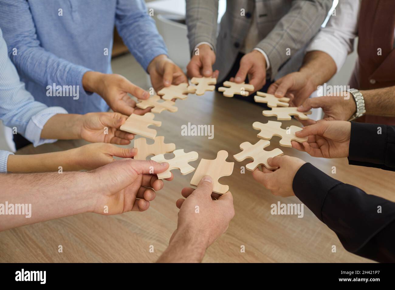 Team von Geschäftsleuten, die um den Bürotisch stehen und Puzzleteile zusammenfügen Stockfoto