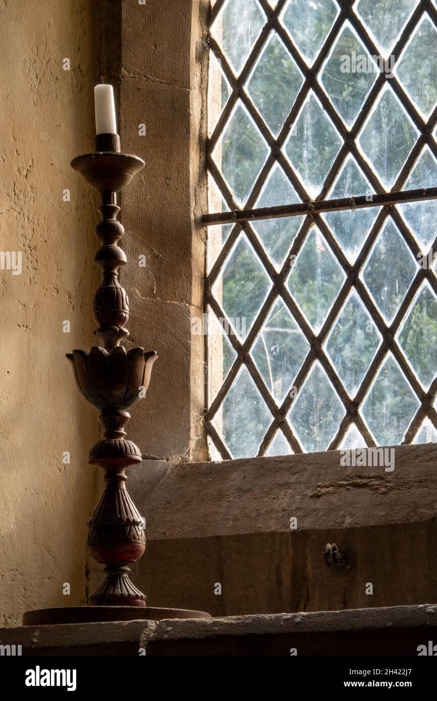 Ein kunstvoller Holzkandelständer auf einem Steinfenstervorsprung mit klassischer Diamantform führt zur St Andrew's Church Boyton, Suffolk Stockfoto