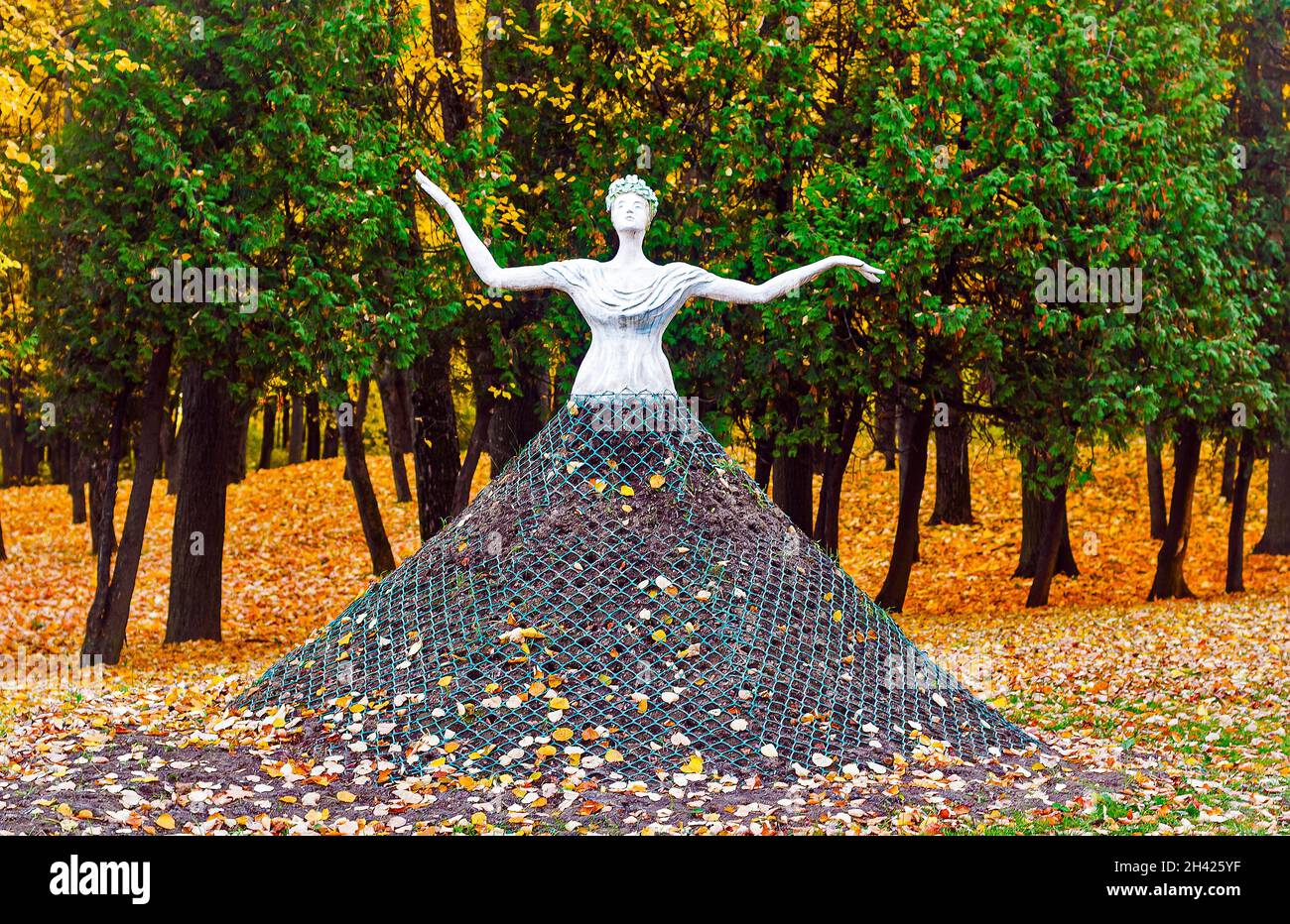 Skulptur eines Mädchens im Herbstpark. Eine alte Statue in einem Stadtpark in einem vollen Rock. Sonniger Tag im Herbstgarten. Stockfoto