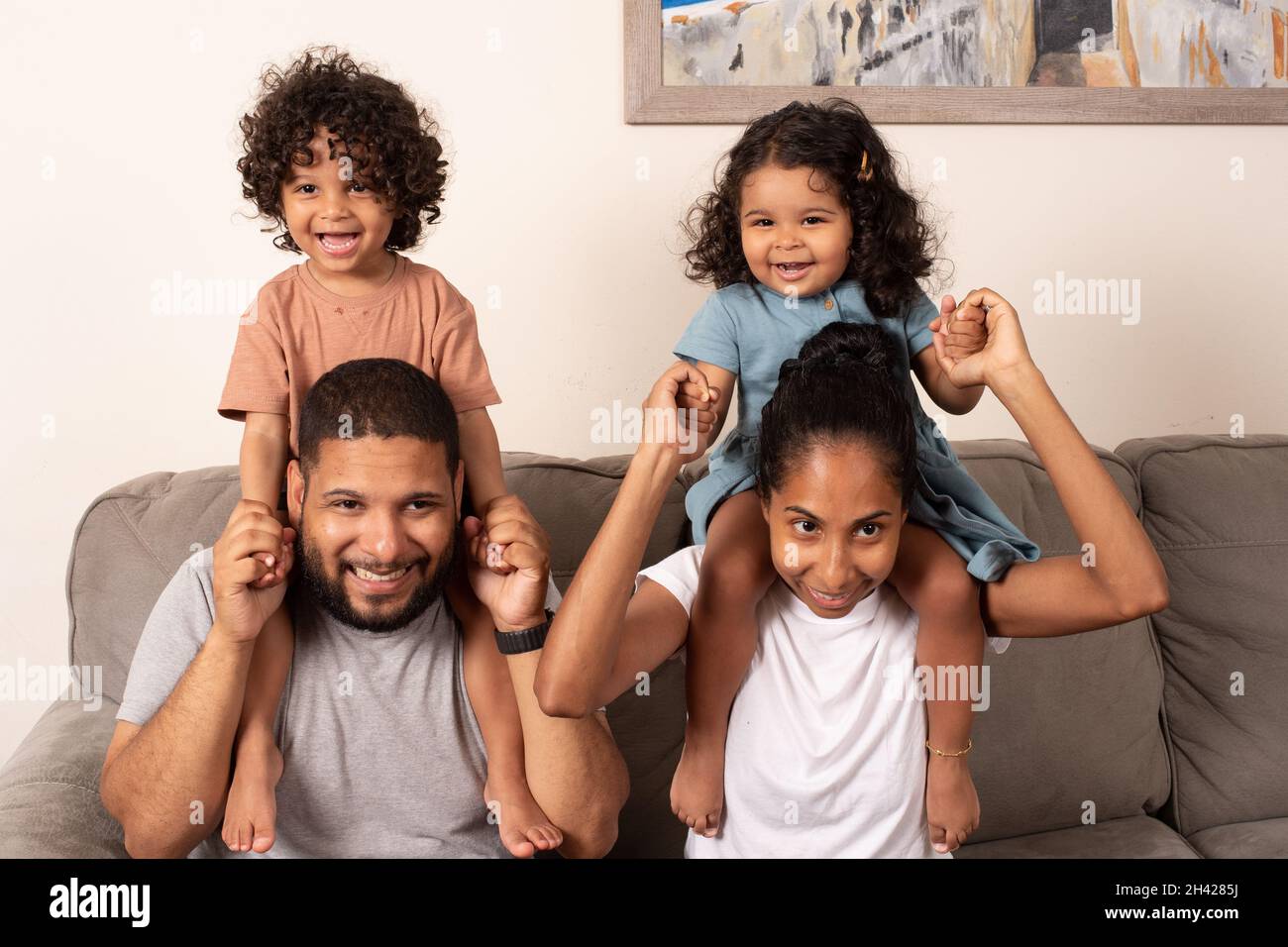 Familienportrait Mutter und Vater mit 2-jährigen brüderlichen Zwillingen, Jungen und Mädchen auf ihren Schultern und lächelnd Stockfoto