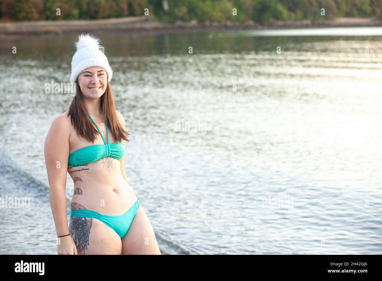 Eine Frau mit Bikini und Wollhut, die an einem Wintertag in der Nähe des Meeres steht und bereit ist, ein kaltes Wasser zu schwimmen Stockfoto