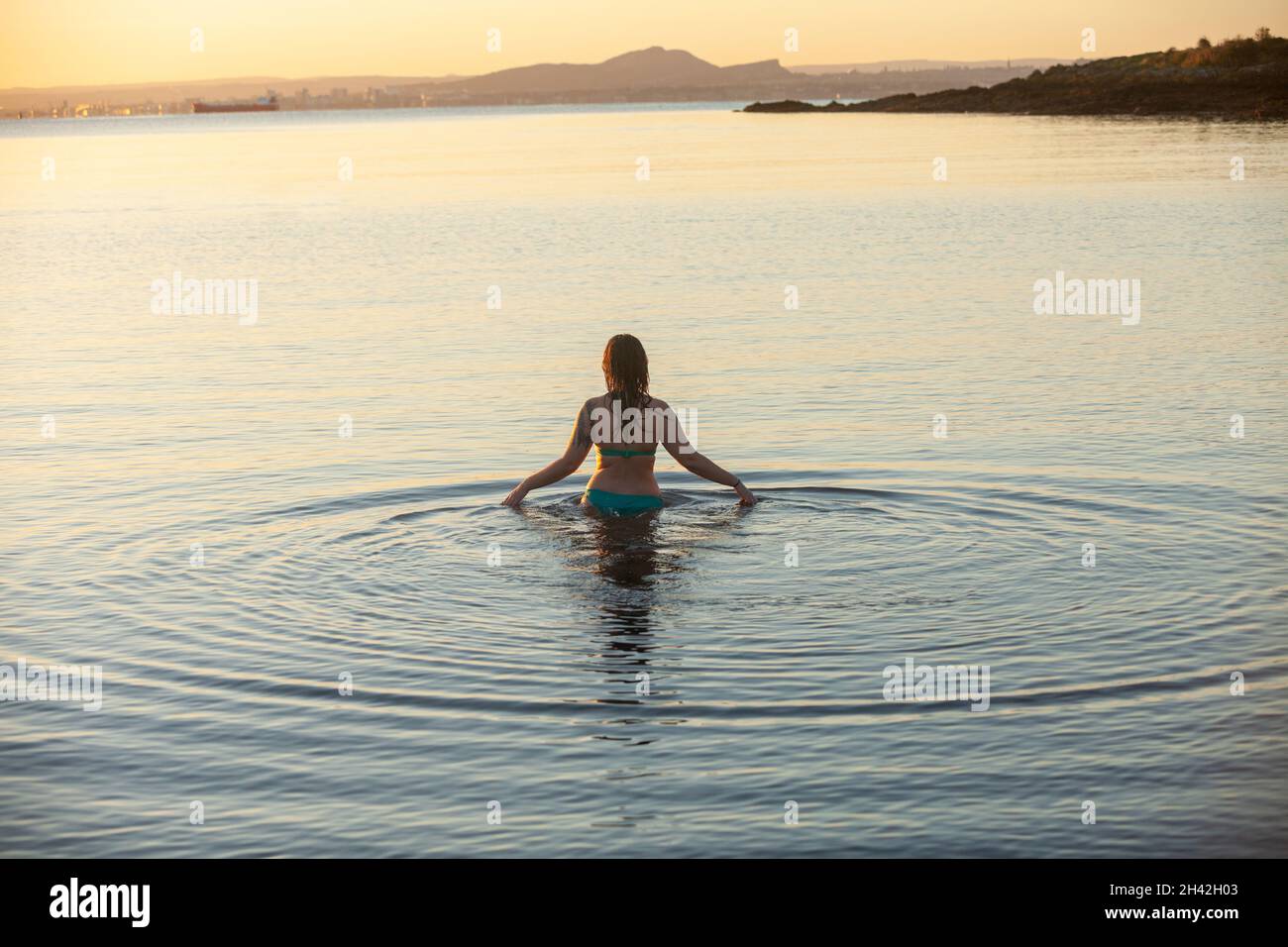 Eine Frau, die bei Aberdour bei einem kalten, aber immer noch aufgehenden Sonnenaufgang im Oktober ins Meer eintrat Stockfoto