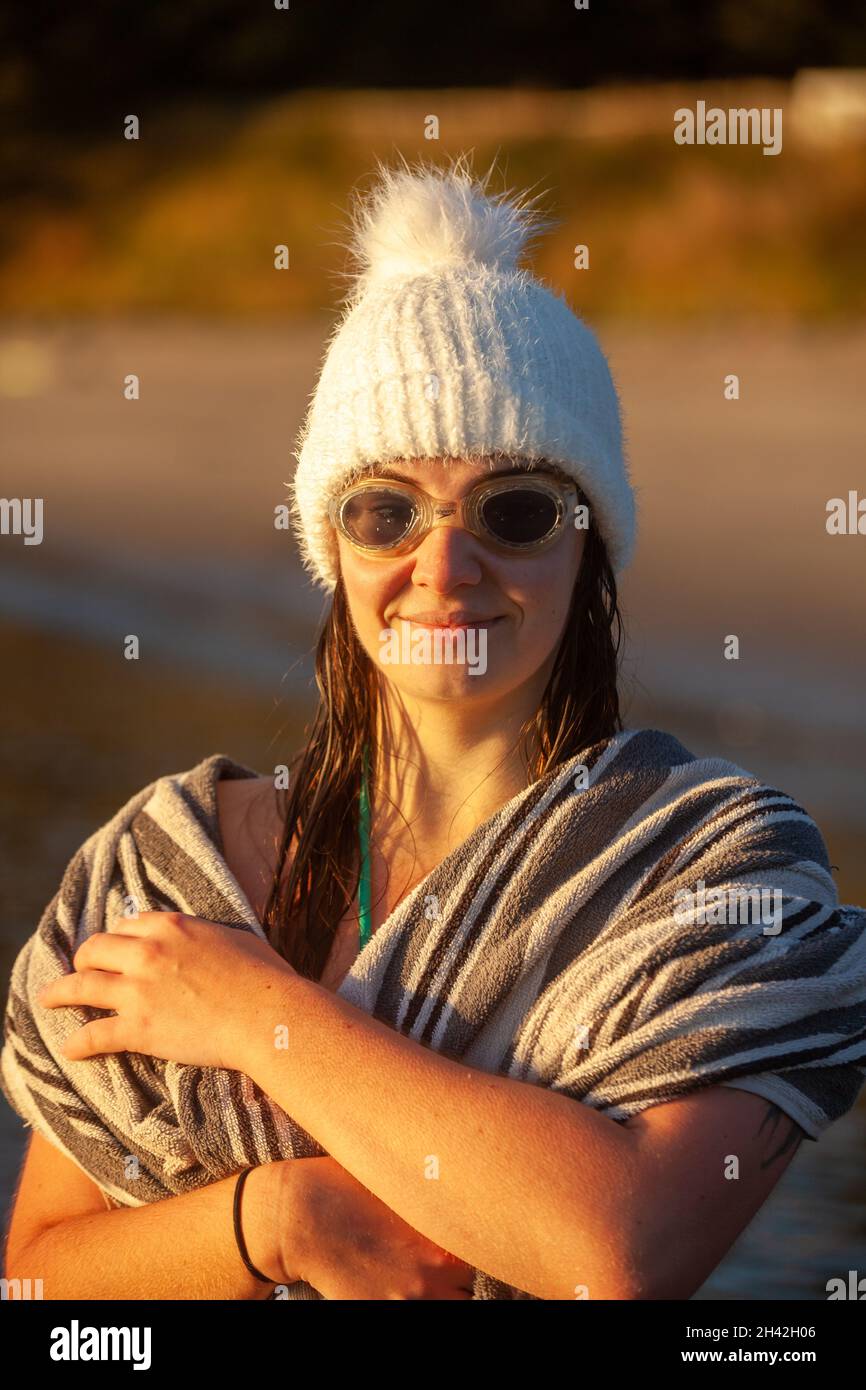 Eine Frau, die einen Wollhut und eine Schwimmbrille trägt, die in ein Handtuch eingewickelt ist, nachdem sie morgens mit kaltem Wasser schwimmen gegangen ist. Stockfoto