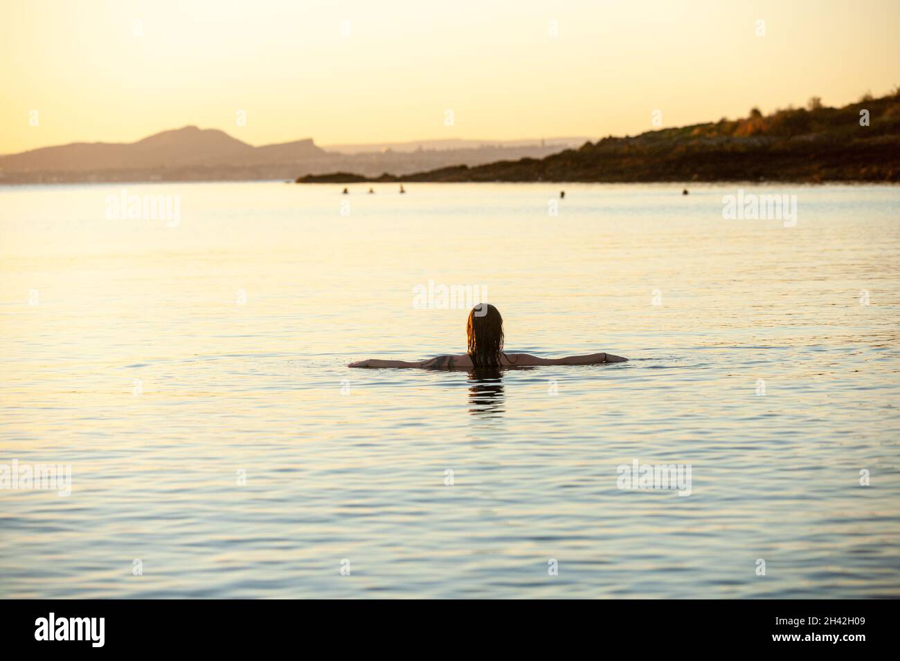 Eine junge schottische Frau, die im Oktober bei Sonnenaufgang im Meer bei Aberdour in Fife, Schottland, schwimmt Stockfoto