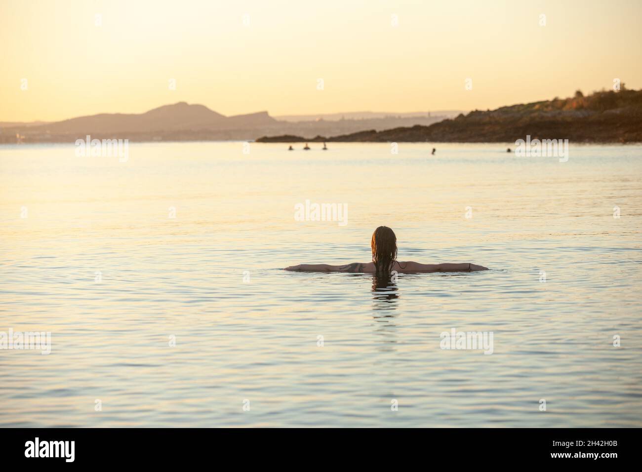 Eine junge schottische Frau, die im Oktober bei Sonnenaufgang im Meer bei Aberdour in Fife, Schottland, schwimmt Stockfoto