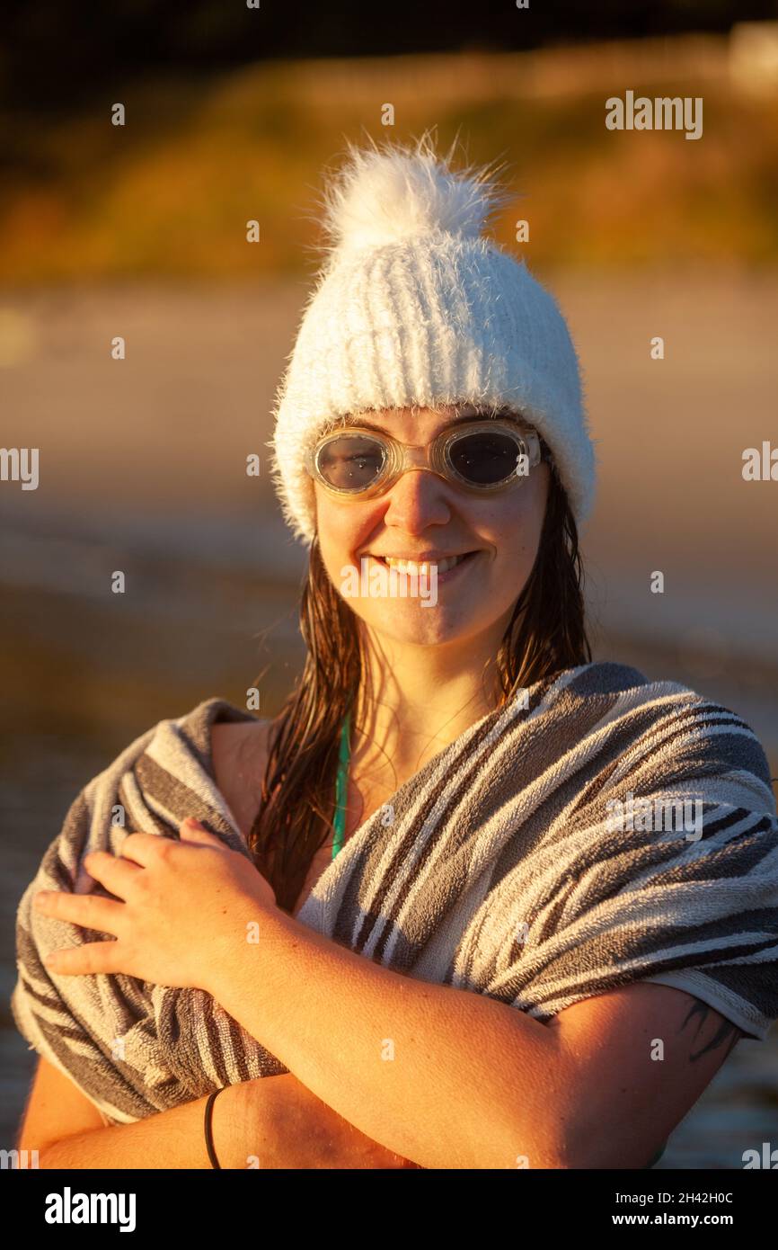 Eine Frau, die einen Wollhut und eine Schwimmbrille trägt, die in ein Handtuch eingewickelt ist, nachdem sie morgens mit kaltem Wasser schwimmen gegangen ist. Stockfoto