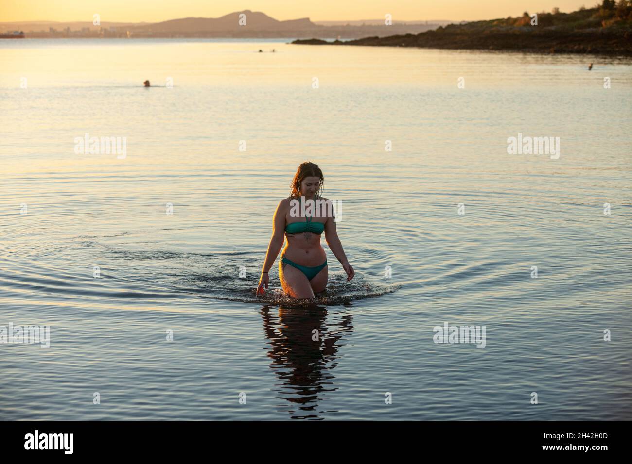 Eine Frau, die einen Bikini trägt und nach einem kalten Wasserschwimmen im Firth of Forth aus dem Meer läuft. Stockfoto