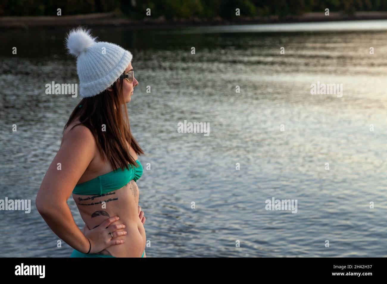 Eine Frau mit Bikini und Wollhut, die an einem Wintertag in der Nähe des Meeres steht und bereit ist, ein kaltes Wasser zu schwimmen Stockfoto