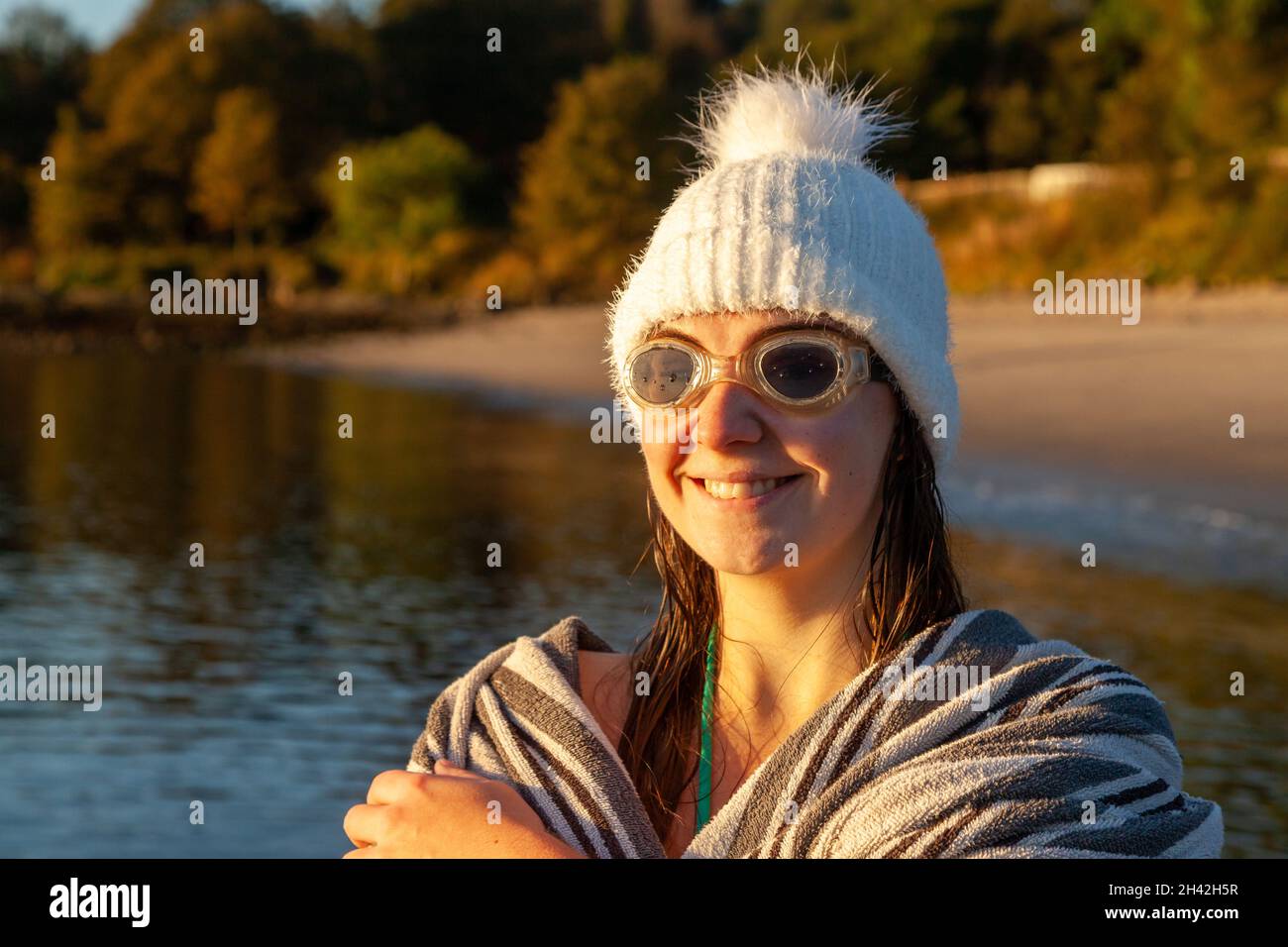 Eine Frau, die einen Wollhut und eine Schwimmbrille trägt, die in ein Handtuch eingewickelt ist, nachdem sie morgens mit kaltem Wasser schwimmen gegangen ist. Stockfoto