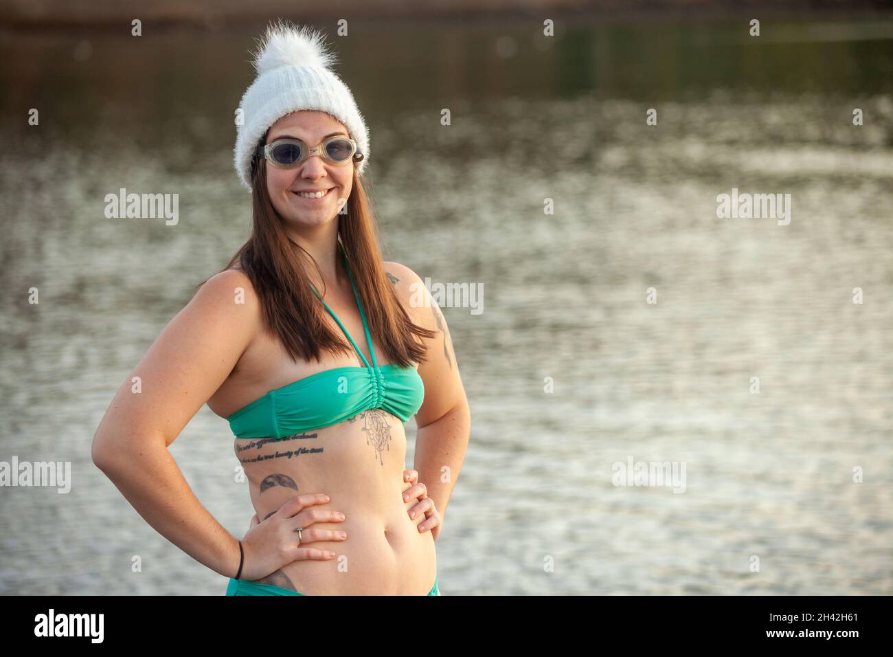 Die junge Frau trägt einen Bikini, einen Wollhut und eine Schwimmbrille neben dem Meer und ist bereit für ein kaltes Bad Stockfoto
