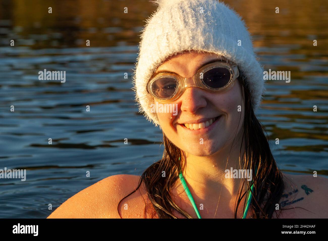 Eine junge schottische Frau, die im Oktober in Aberdour, Fife, Schottland, im Meer schwimmt und einen weißen Wollhut mit kaltem Wasser trägt Stockfoto