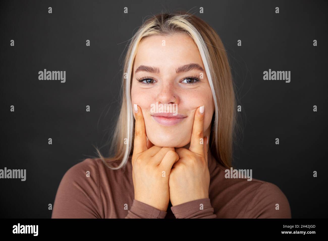 Porträt einer jungen Frau, die ihre Finger in ihre Wangen drückt und sie zum Lächeln bringt Stockfoto