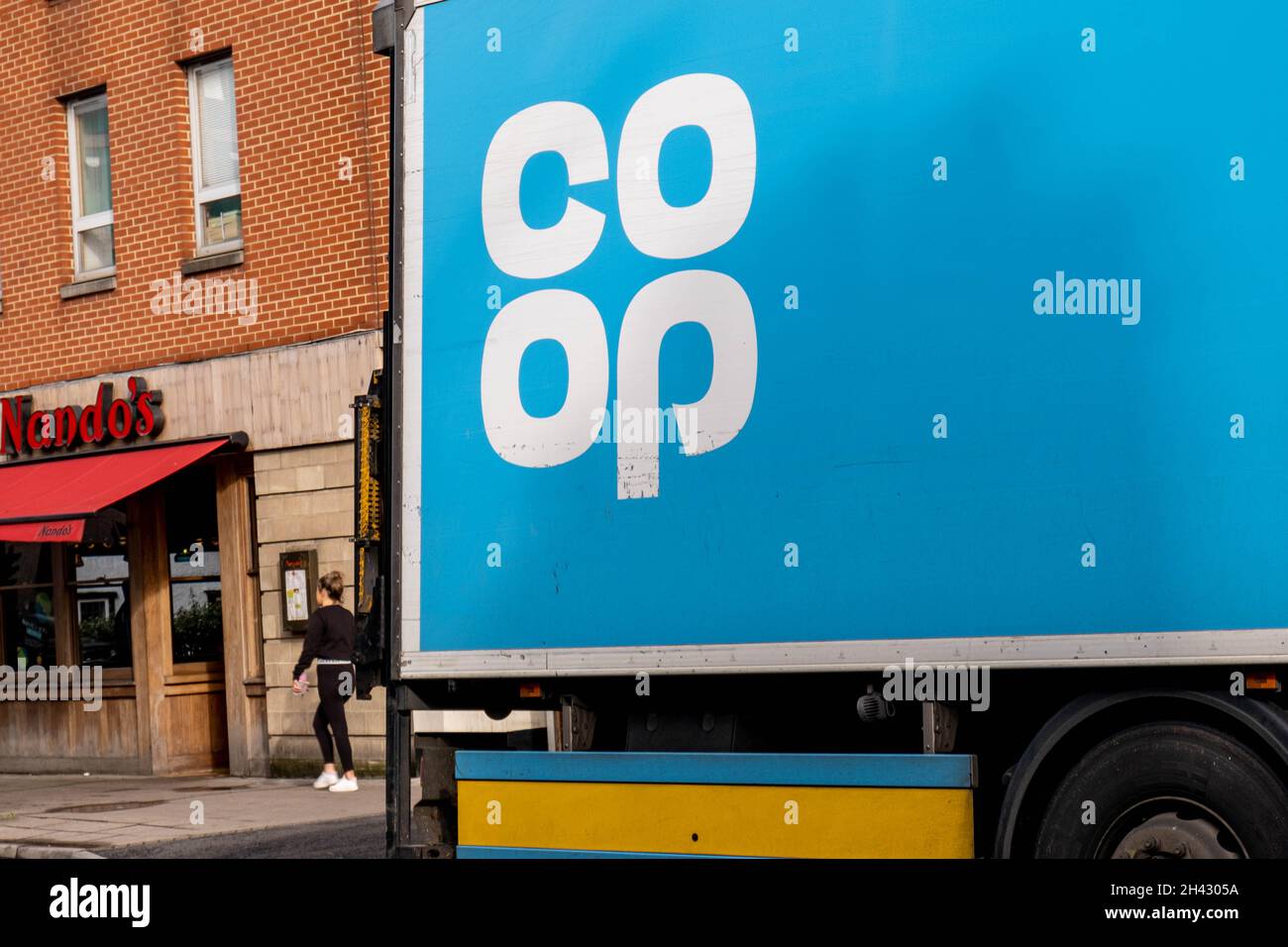 Epsom Surrey London, Großbritannien, Oktober 31 2021, Co-Op Food Delivery Truck oder LKW, der an Einem Nando's Restaurant vorbeifährt und an Dem Eine Frau vorbeiläuft Stockfoto