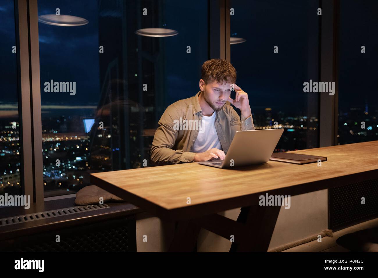 Nachdenklicher junger Mann, der spät im Büro online am Computer arbeitet. Stockfoto